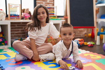 Brother and sister smiling confident sitting on floor at kindergarten