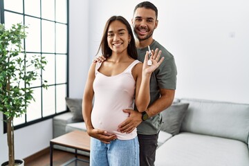 Latin man and woman couple hugging each other holding key of new house expecting baby at home