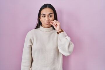 Young south asian woman standing over pink background mouth and lips shut as zip with fingers....