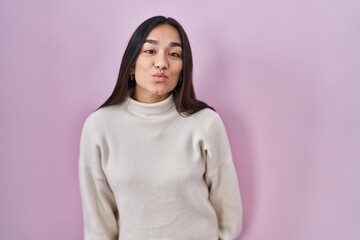 Fototapeta premium Young south asian woman standing over pink background looking at the camera blowing a kiss on air being lovely and sexy. love expression.