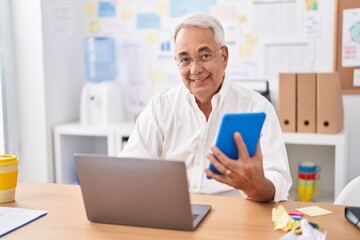 Middle age grey-haired man business worker using touchpad and laptop at office