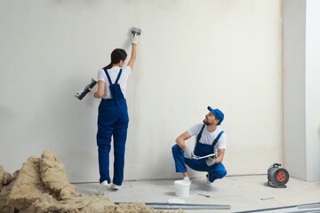 Professional workers plastering wall with putty knives indoors - obrazy, fototapety, plakaty