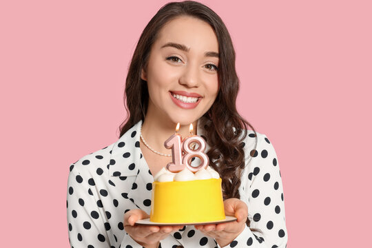 Coming of age party - 18th birthday. Smiling woman holding delicious cake with number shaped candles on pink background