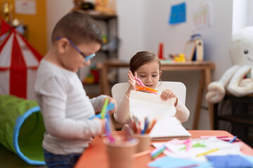 Adorable girl and boy sitting on table cutting paper at kindergarten