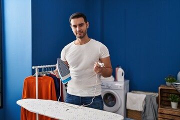 Young hispanic man with beard ironing clothes at home relaxed with serious expression on face. simple and natural looking at the camera.