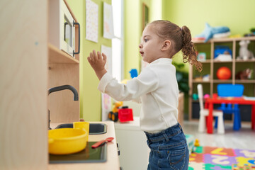 Adorable blonde girl playing with play kitchen standing at kindergarten