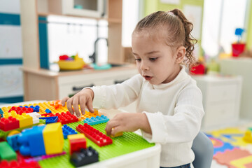 Adorable blonde girl playing with construction blocks sitting on table at kindergarten