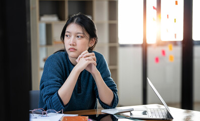 Serious young woman sitting at home office, deep in thoughts, thinking concept