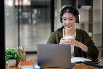 Young attractive university student with headphone using laptop computer, studying at modern...