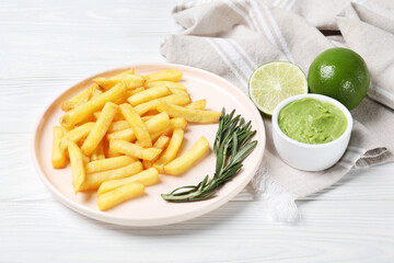 Plate with french fries, avocado dip, rosemary and lime served on white wooden table