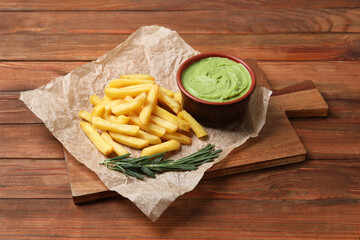 Serving board with parchment, french fries, avocado dip and rosemary on wooden table