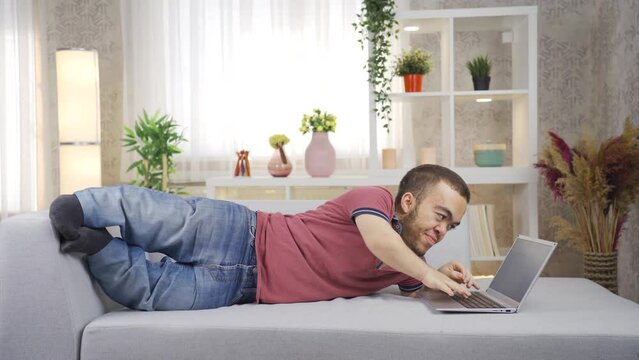 A man with dwarfism works from home on a laptop.
Young man with dwarfism is using laptop at home, happy and smiling.
