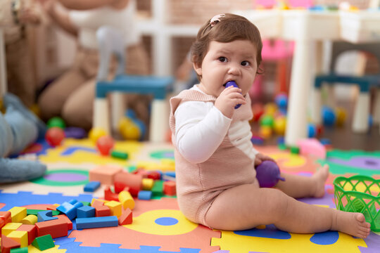 Adorable Toddler Bitting Plastic Food Toy Sitting On Floor At Kindergarten