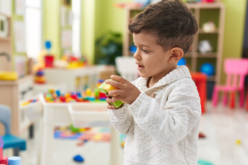 Adorable hispanic toddler playing with construction blocks standing at kindergarten