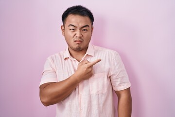 Chinese young man standing over pink background pointing aside worried and nervous with forefinger,...