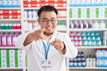 Chinese young man working at pharmacy drugstore pointing to you and the camera with fingers, smiling positive and cheerful