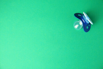 Blue baby pacifier on green background, top view. Space for text