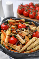 Tasty roasted baby corn with tomatoes, capers and mushrooms on table, closeup