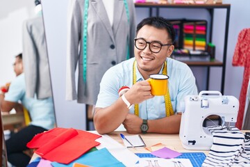 Young chinese man tailor smiling confident drinking coffee at tailor shop
