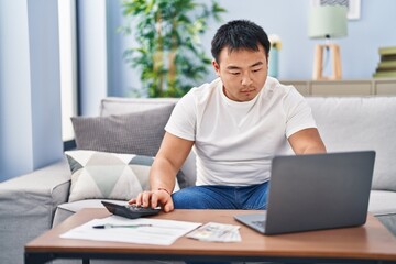 Young chinese man accounting economy using laptop and calculator at home