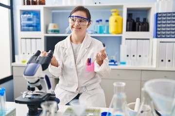 Fototapeta premium Hispanic girl with down syndrome working at scientist laboratory doing money gesture with hands, asking for salary payment, millionaire business