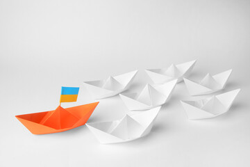 Group of paper boats following orange one on white background. Leadership concept