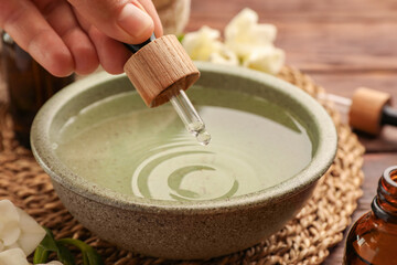 Woman dripping essential oil into bowl at wooden table, closeup. Aromatherapy treatment