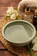 Obraz na płótnie Canvas Bowl of essential oil and beautiful flowers on wooden table. Aromatherapy treatment