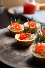 Delicious tartlets with red caviar and cream cheese served on wooden board, closeup