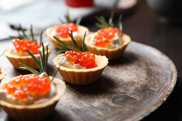 Delicious tartlets with red caviar and cream cheese served on wooden board, closeup