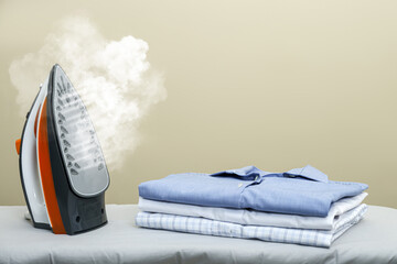 Modern iron with steam and folded clothes on ironing board, space for text