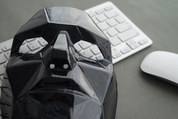 Black scary half face mask, keyboard and mouse on gray table background in dark tone. Hacker,...