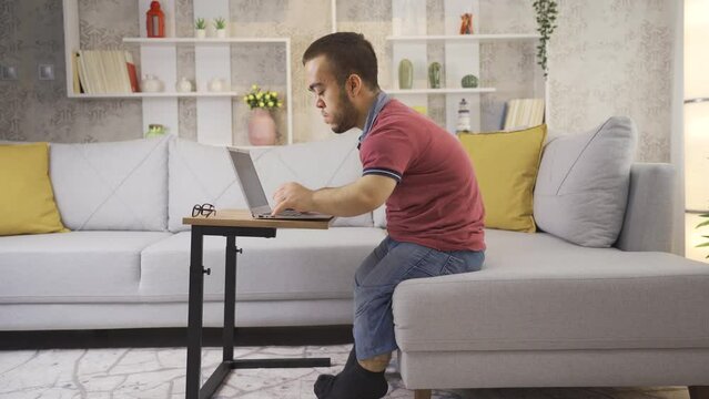Young male student with dwarfism studying at home using laptop.
College student young man with dwarfism studying at home, disabled young student using laptop.
