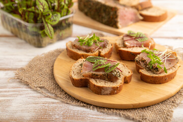 Bread sandwiches with jerky salted meat, sorrel and cilantro microgreen on white. side view, selective focus.