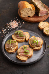 Bread sandwiches with jerky salted meat, sorrel and cilantro microgreen on black. side view.