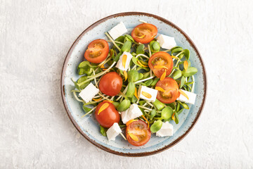 Vegetarian salad of tomatoes, marigold, microgreen, feta cheese on gray. Top view.