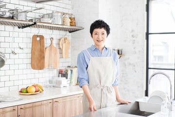 明るく広い清潔なキッチンにエプロンをつけて立つアジア人女性、ミドル世代