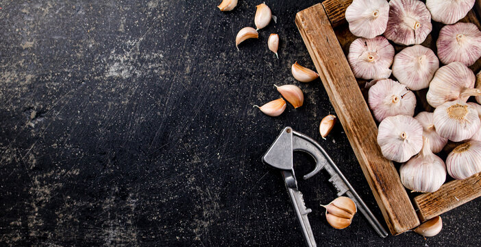 Garlic on a wooden tray with a garlic press.