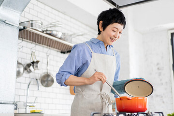 愛情込めて料理をしている女性、鍋の蓋を開けて様子を見ている © lielos