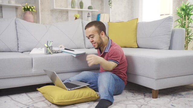 Young male student with dwarfism studying at home using laptop. College student young man with dwarfism studying at home, disabled young student using laptop.
