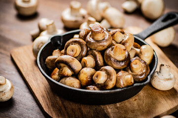 Fried mushrooms in a frying pan on a cutting board. 