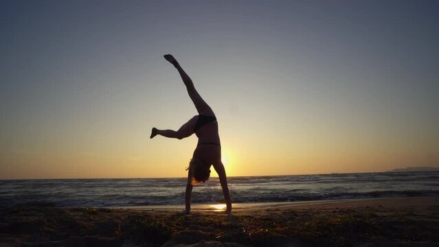 Young athletic woman doing balancing handstand exercise on beach sunset, slow motion