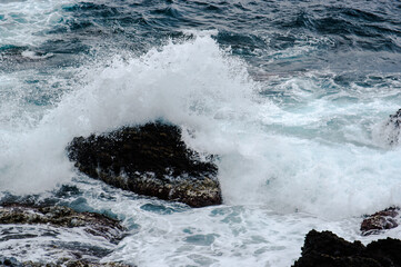 海面に出ている岩に波が押し寄せて波が砕ける様子