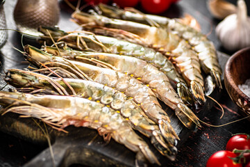 Raw shrimp on a cutting board with spices and tomatoes. 