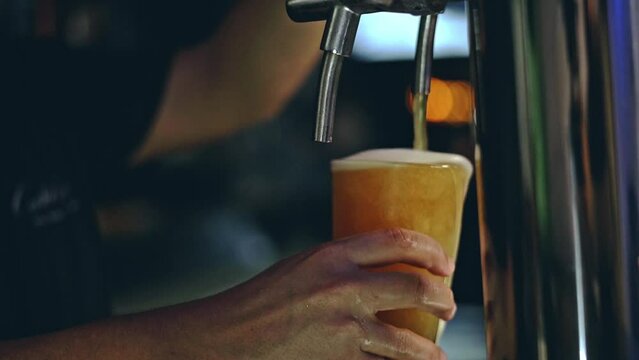 image of an unrecognizable man pouring a cold craft beer into a beer glass at a night bar
