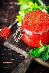 A full glass jar of red caviar on a cutting board. 