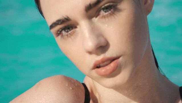 Charming girl with black eyebrows, thick eyelashes and wet hair in swimming pool