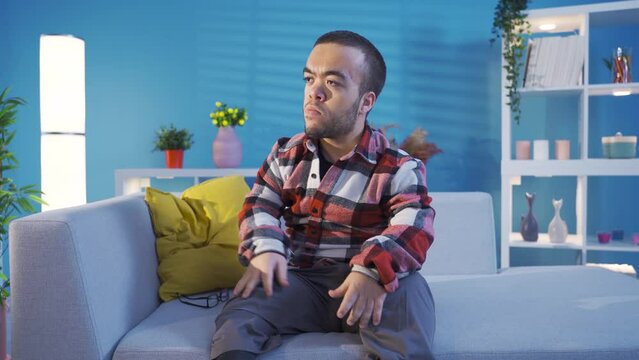 Young man with disabled dwarfism sitting on the sofa at home becomes angry and aggressive.