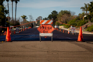 Traffic sign stating Fresh Oil with asphalt slurried road in the background