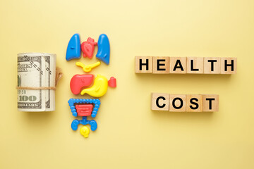 Flatlay picture of fake cash, toy organ and wooden block written health cost.